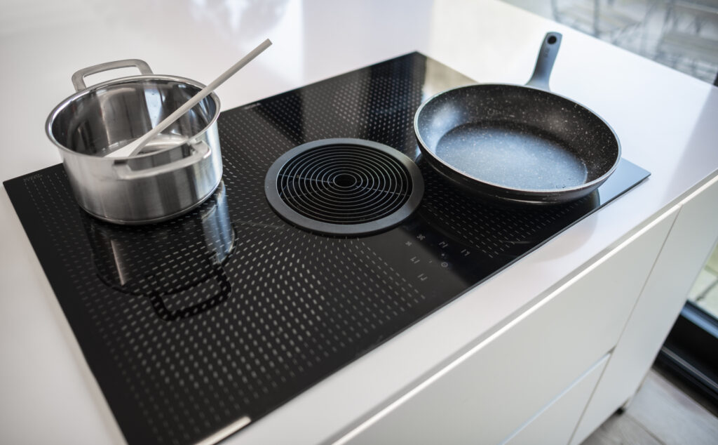 Une casserole en acier inoxydable avec une cuillère blanche et une poêle noire sont posées sur une plaque de cuisson moderne.