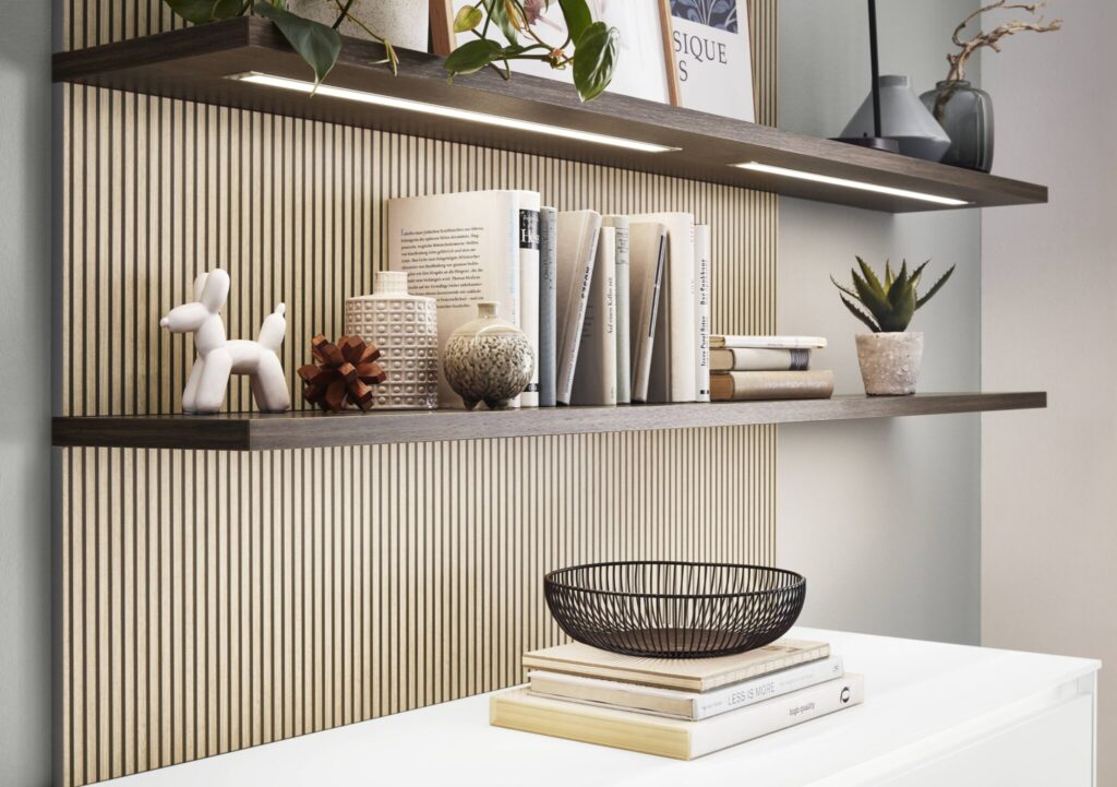 Étagères en bois avec objets décoratifs, livres, sculpture blanche, plantes en pot, et panier noir, éclairées par des lumières intégrées.