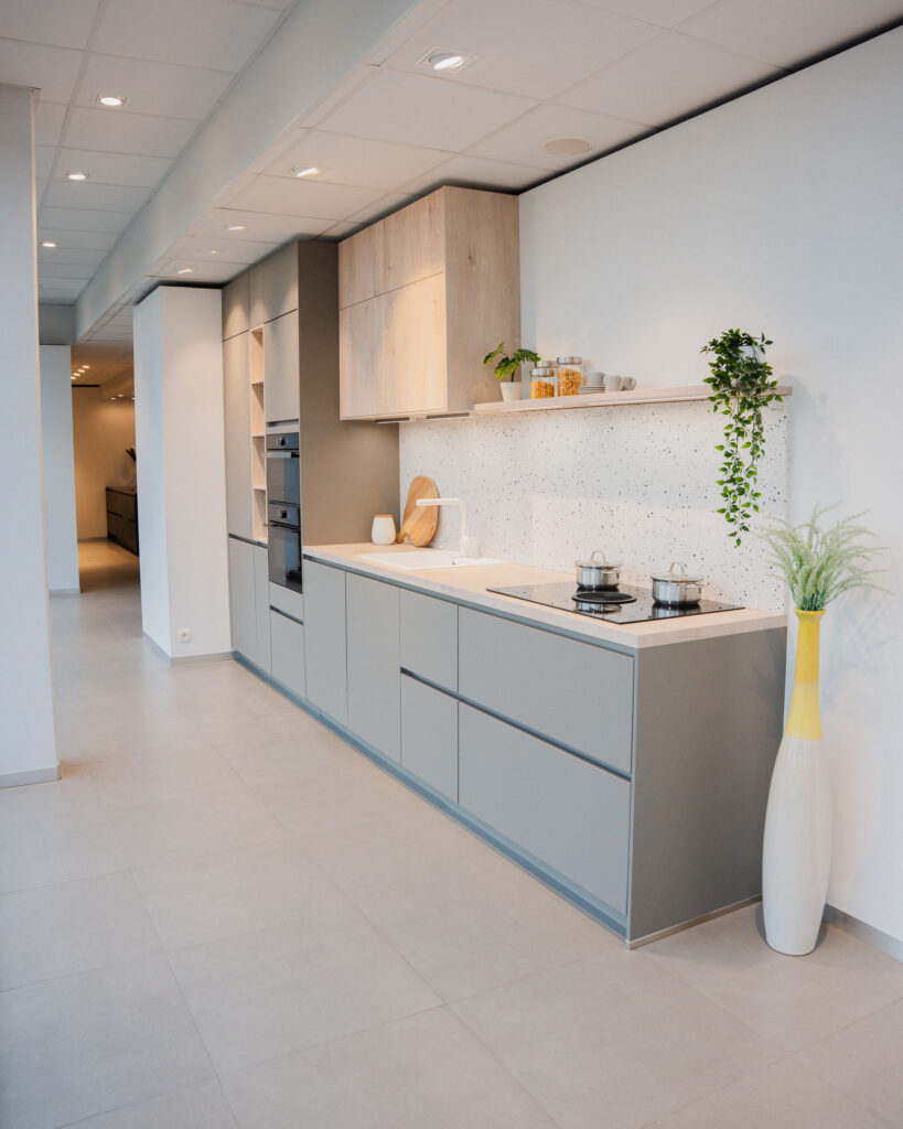 Cuisine moderne avec meubles bas gris, armoires hautes en bois clair, plan de travail blanc, évier, plaque de cuisson noire et deux casseroles.