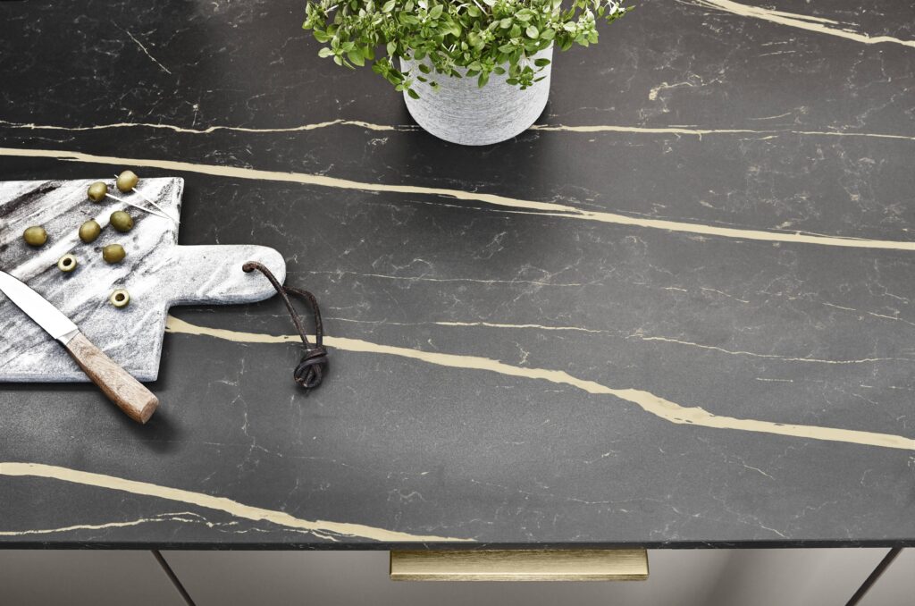 Plan de travail en marbre noir avec des veines dorées, une planche à découper en marbre, des olives et un couteau.