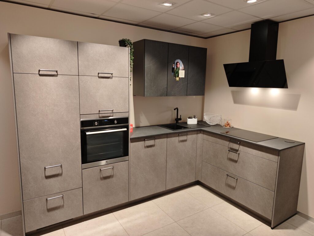 Cuisine moderne avec placards gris, four encastré, hotte noire, évier noir et comptoirs en pierre, éclairée par des spots au plafond.