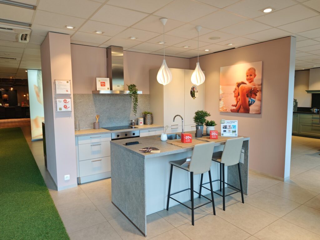Cuisine moderne avec îlot central gris, deux chaises beige, luminaires suspendus blancs et un tableau mural d'une mère et son enfant.