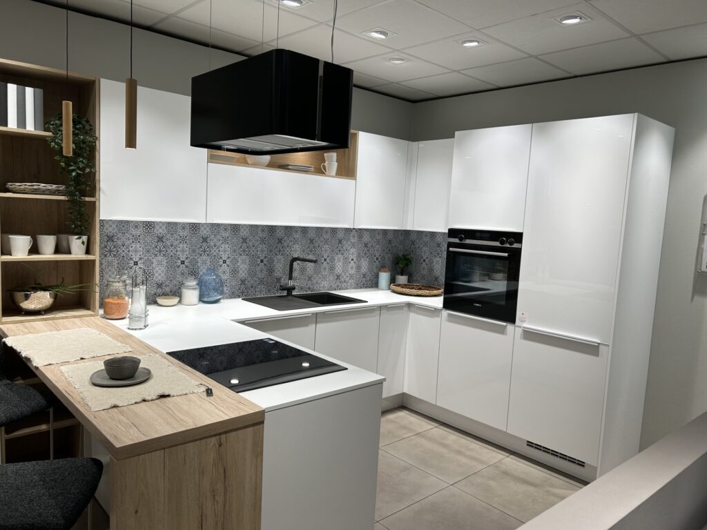 Cuisine avec des façades blanches avec crédence à motifs. Plan de travail blanc, évier noir, hotte noire suspendue.