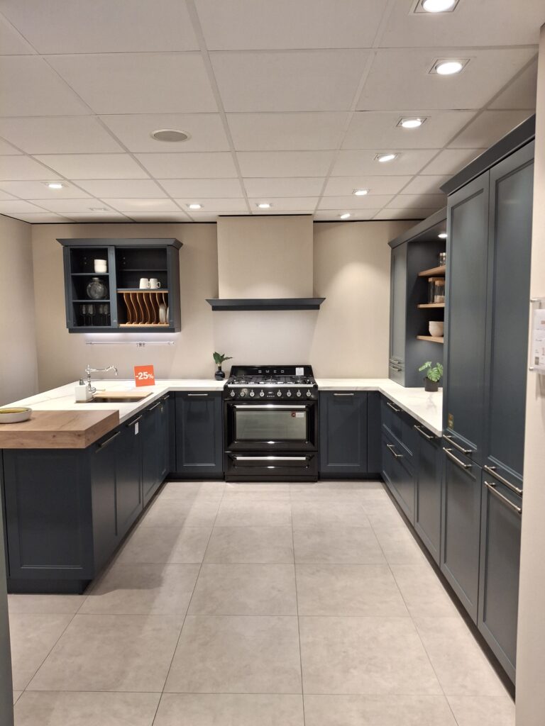 Cuisine cottage aux façades bleu fjord avec cuisinière noire. Plan de travail effet marbre blanc et corniches.