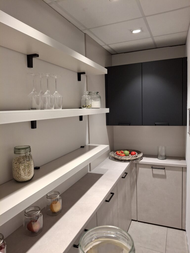 Arrière-cuisine avec étagères blanches, meubles de rangement bas en effet béton sable fin et meubles de rangement hauts aux façades noir mat.