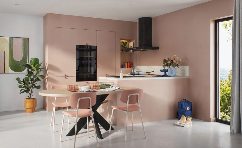Cuisine moderne rose en L, avec une table appuyéeavec pied centrale et 4 chaises roses