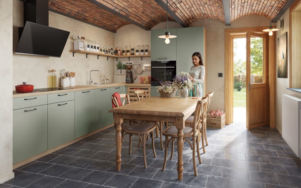 Cuisine équipée aux meubles vert sauge et plan de travail en bois, avec table en bois, chaises, hotte noire, étagères et porte vitrée ouverte.