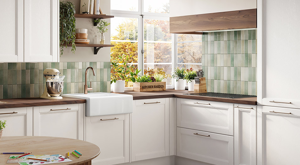 Cuisine en L avec meubles blancs, plan de travail en bois foncé, crédence en carreaux vert clair, évier blanc sous la fenêtre et étagères murales.
