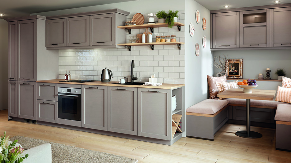 Cuisine campagnarde avec meubles gris taupe, crédence en carreaux blancs, étagères en bois, évier noir et coin repas avec banquettes et table en bois.