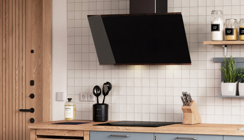 Hotte noire inclinée fixée sur un mur en carreaux blancs, au-dessus d’une plaque de cuisson noire sur un plan de travail en bois.