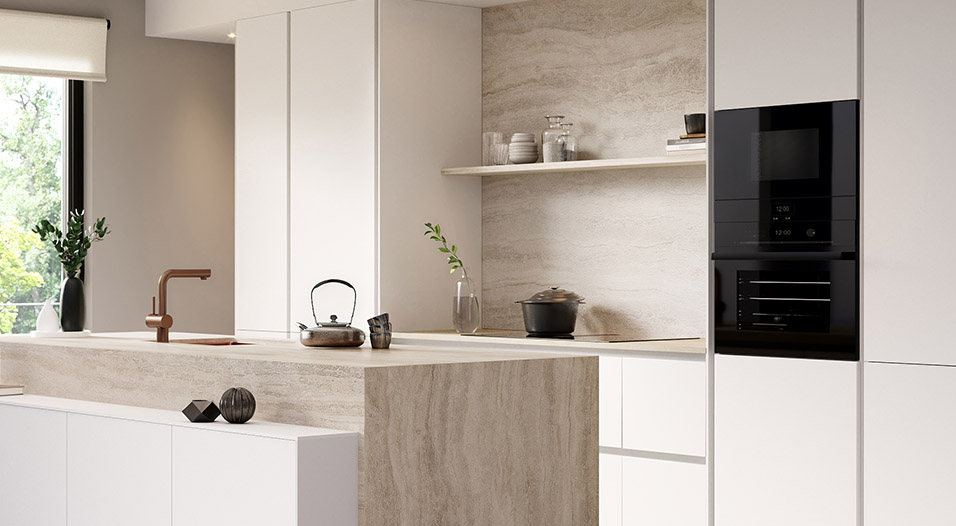 Cuisine moderne avec îlot central en pierre beige, meubles blancs, robinet cuivré, étagère murale décorée et colonne de fours noirs à droite.