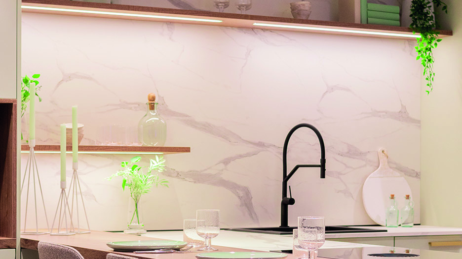Cuisine moderne avec crédence effet marbre blanc et gris, robinet noir central, étagères en bois, plantes vertes, bougies blanches et vaisselle posée au premier plan.