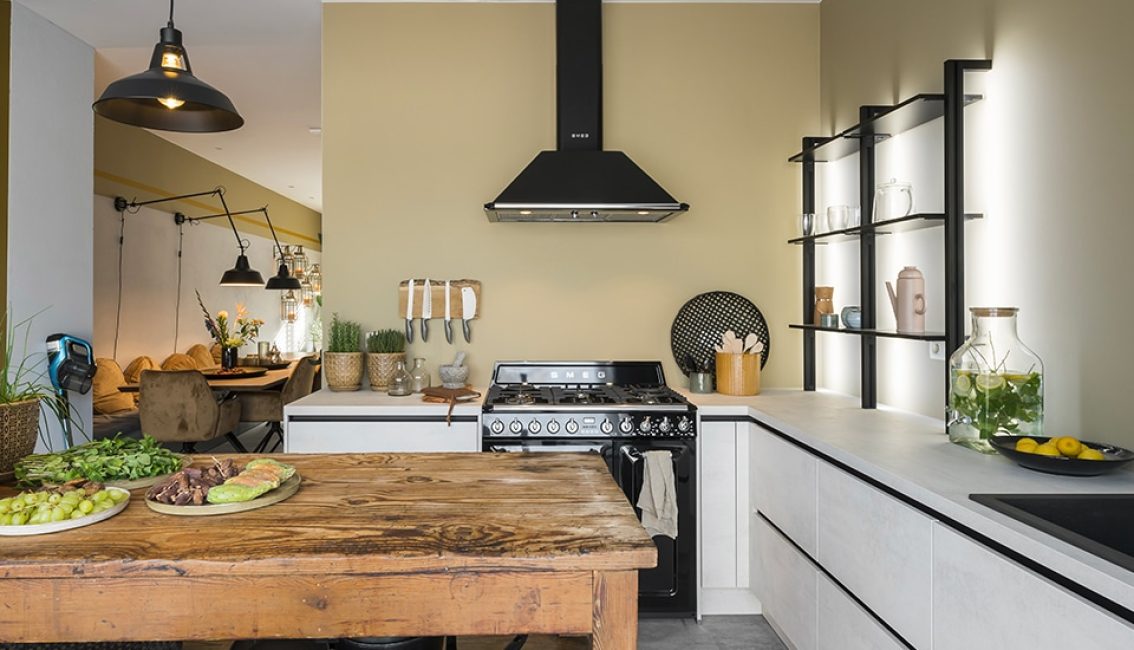Cuisine moderne avec un îlot en bois, une cuisinière noire, des étagères éclairées, et des fruits sur le plan de travail.