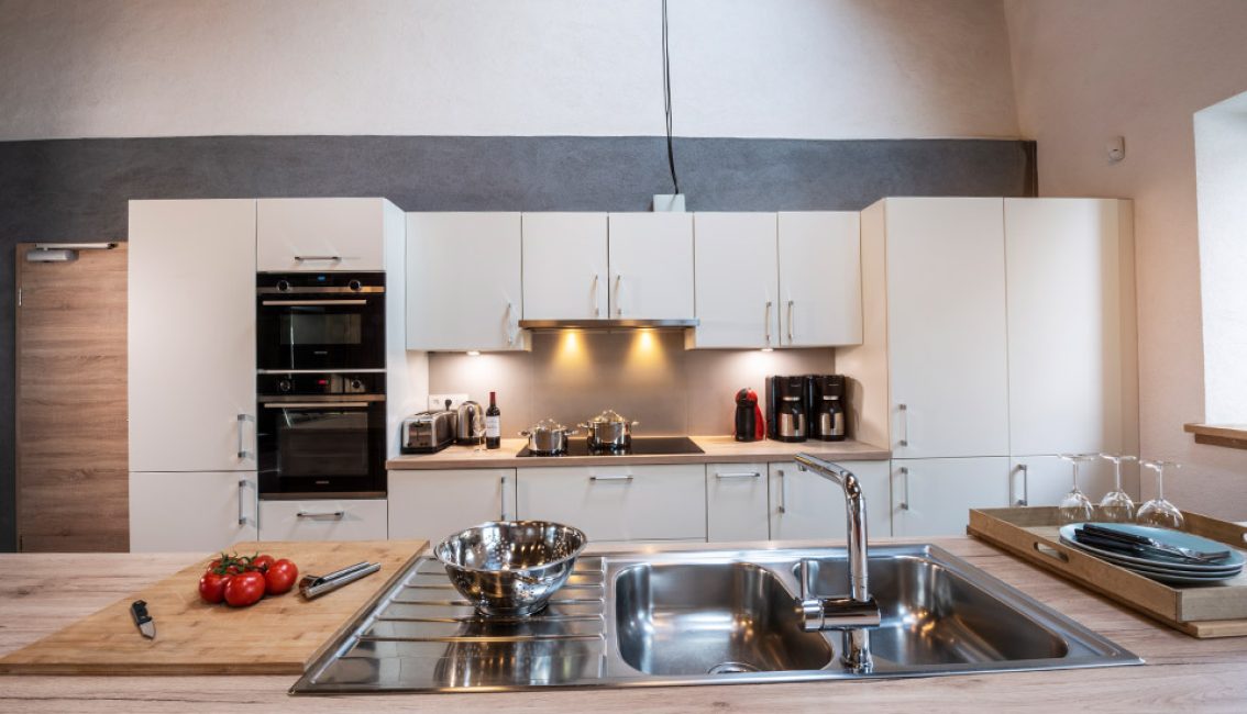Cuisine moderne avec des placards blancs, un plan de travail en bois clair, des appareils électroménagers en acier inoxydable et des tomates sur une planche à découper.