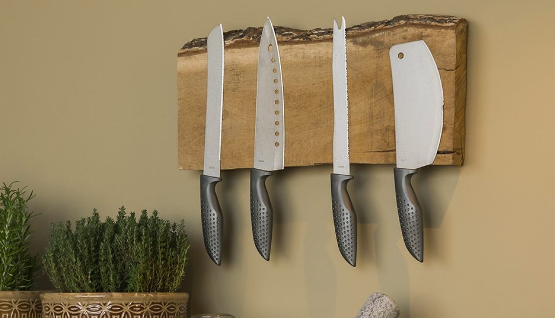 Quatre couteaux de cuisine aux manches noirs sont fixés sur un support en bois au mur, avec des plantes en pot en dessous.