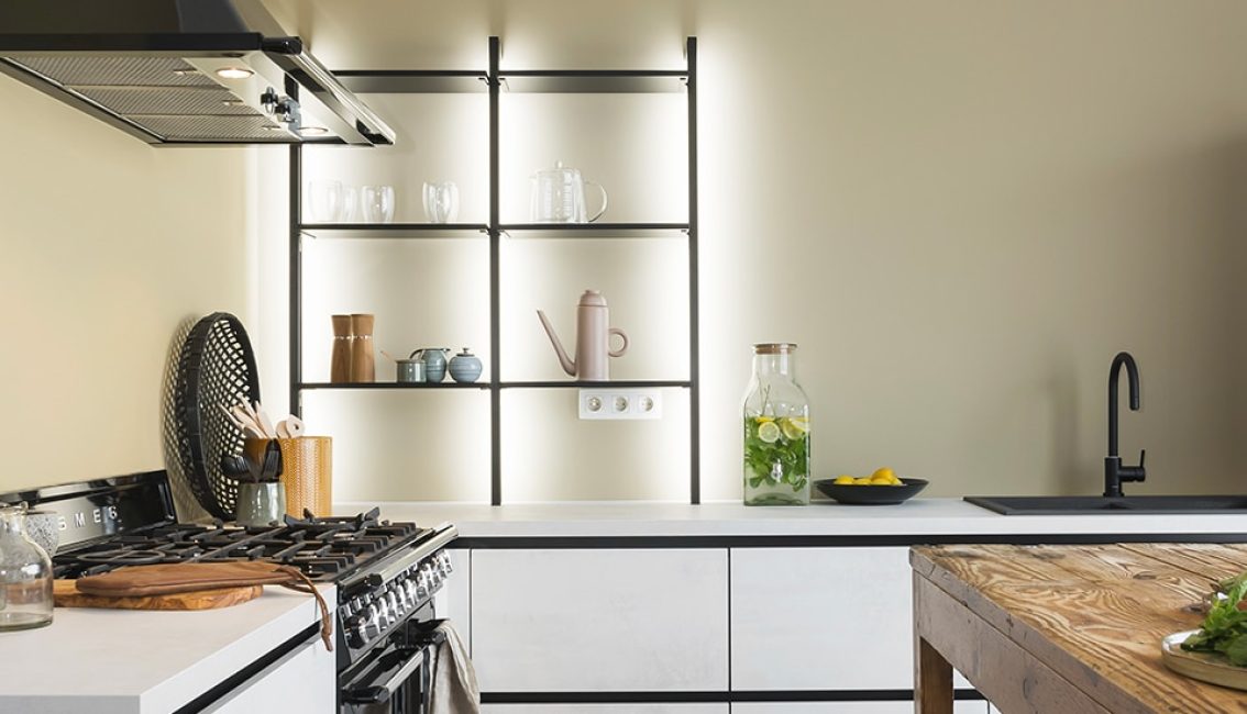 Cuisine moderne avec étagères noires, carafe d'eau citronnée, bol de citrons, plan de travail clair et cuisinière à gaz.