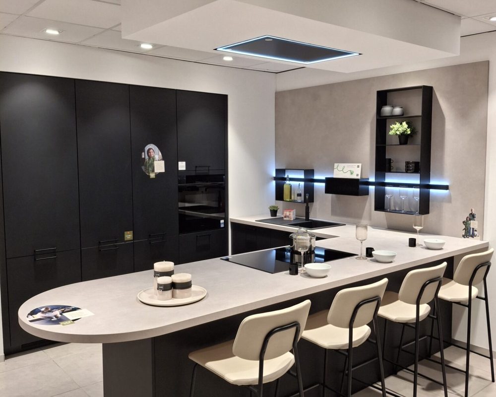 Cuisine aux façades noires, avec îlot central avec 4 chaises. PLan de travail gris.