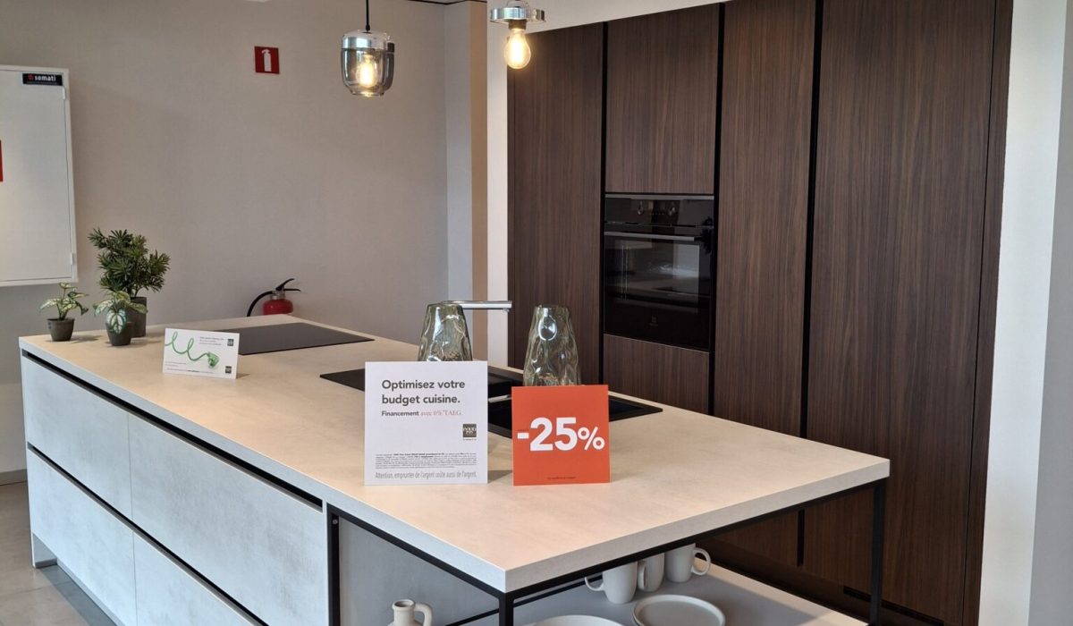 Cuisine avec meubles encastrés en bois foncé, et grand îlot central avec façade effet béton blanc et plan de travail blanc. Hotte au plafond.