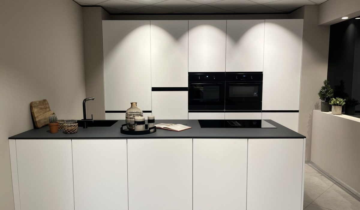 Cuisines aux façades blanches et mattes, avec îlot central et plan de travail noir. Évier et électroménagers noirs.