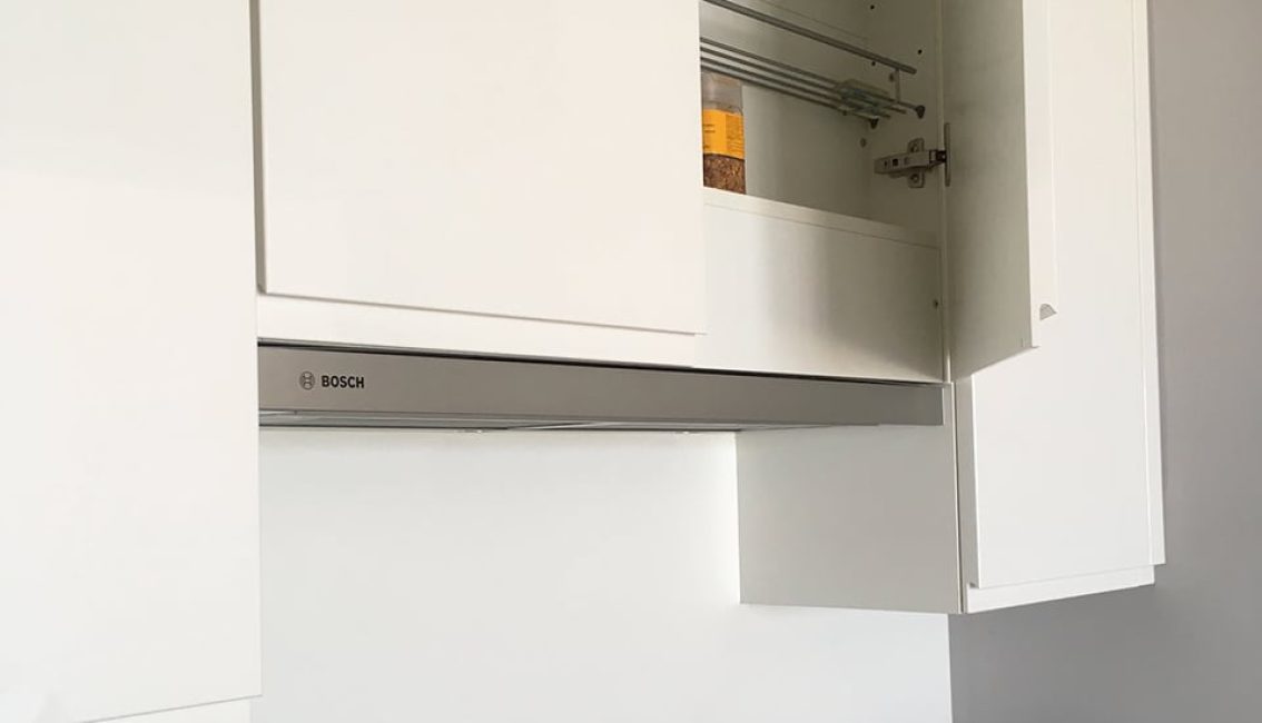 Un placard de cuisine blanc ouvert révèle un pot de nourriture sur l'étagère, avec une hotte Bosch visible en dessous.