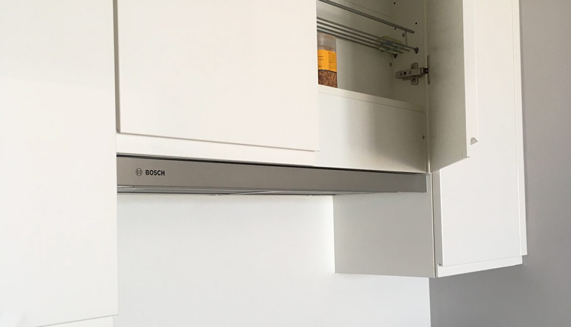 Un placard de cuisine blanc ouvert révèle un pot de nourriture sur l'étagère, avec une hotte Bosch visible en dessous.