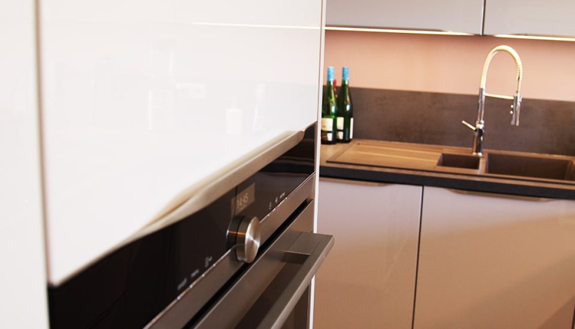 Four encastré moderne en acier inoxydable à gauche, évier avec robinet chromé et bouteilles vertes sur le plan de travail à droite.