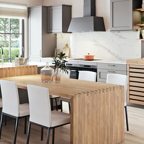 Cuisine moderne avec armoires grises, plan de travail et table en bois clair, quatre chaises blanches, hotte noire, étagères ouvertes et évier devant une fenêtre.